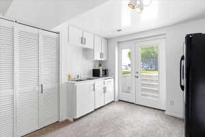Compact kitchen space featuring white cabinetry, a double basin sink, and a black refrigerator