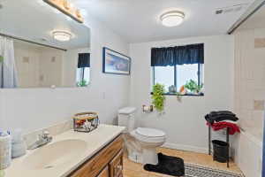 Bathroom featuring a single-sink vanity with light-colored countertop and wood-finish cabinetry, a window with black privacy curtain, a toilet, and a tiled shower/tub combination