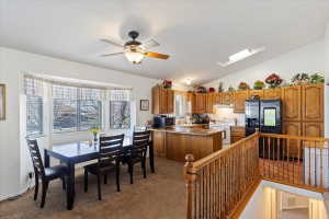 Carpeted dining area featuring a bay window, ceiling fan with light fixture, and wood railing