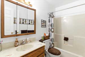 Bathroom featuring a wood-finish vanity with an integrated sink and light-toned countertop, a three-panel mirrored medicine cabinet, and a shower/tub combination with a white surround