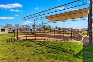 Outdoor arena with a metal frame shade structure, perimeter fencing, and a sand base