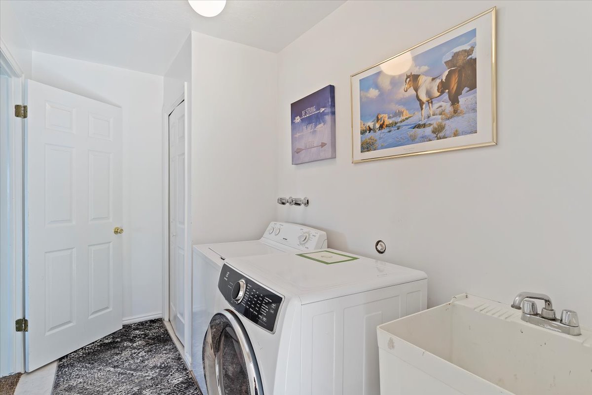 Dedicated laundry area featuring a front-load washing machine, a top-load washing machine, and a utility sink with a chrome faucet