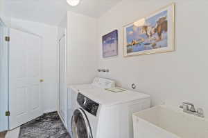 Dedicated laundry area featuring a front-load washing machine, a top-load washing machine, and a utility sink with a chrome faucet