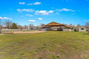 Expansive green space featuring a covered outdoor structure, a fenced arena, a detached shed, and a mountain backdrop