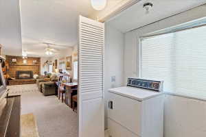 Dedicated laundry area with a large window and louvered bifold door, offering direct access to a carpeted living space featuring a brick fireplace with an insert and ceiling fans