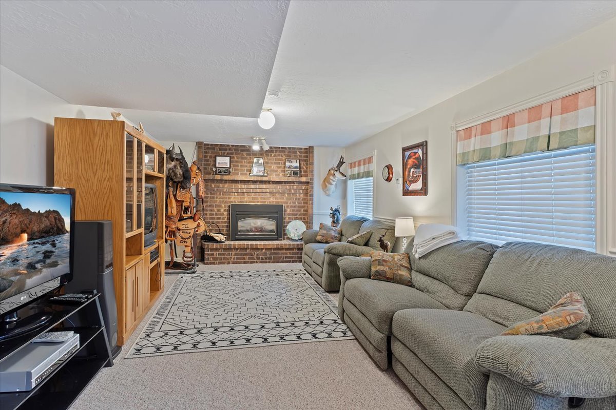 Spacious living area featuring a prominent brick fireplace with a dark metal insert, carpet flooring, multiple windows with blinds, and recessed ceiling lighting