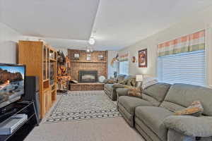 Spacious living area featuring a prominent brick fireplace with a dark metal insert, carpet flooring, multiple windows with blinds, and recessed ceiling lighting