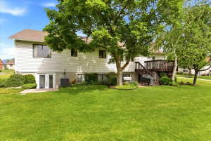 Expansive grassy backyard featuring mature trees, a multi-level wood deck, and a walk-out basement with double doors
