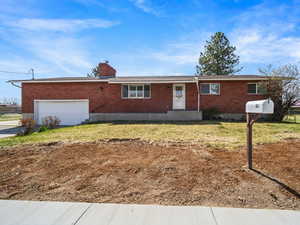 Single story home featuring a front yard, brick siding, a chimney, a garage, and driveway