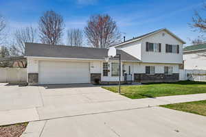 View of front of home featuring an attached garage, fence, brick siding, a front lawn, and driveway