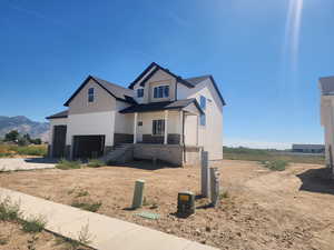 View of front of home with covered porch, a garage, driveway, stone siding, and a mountain view