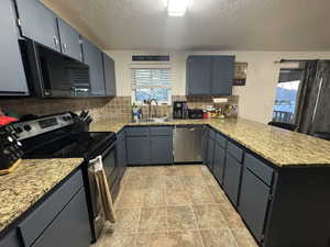 Kitchen featuring tasteful backsplash, a sink, appliances with stainless steel finishes, a peninsula, and a textured ceiling