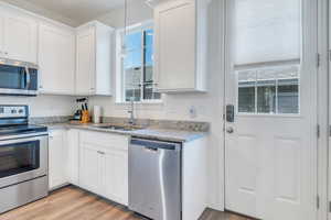 Kitchen with a sink, white cabinets, light wood finished floors, and stainless steel appliances