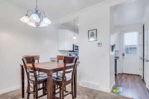 Dining area with a notable chandelier, visible vents, baseboards, and crown molding