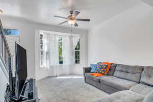 Carpeted living room featuring baseboards, a textured ceiling, a ceiling fan, crown molding, and stairs