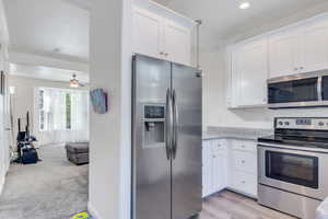 Kitchen featuring ceiling fan, white cabinetry, light carpet, appliances with stainless steel finishes, and open floor plan