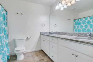 Full bathroom featuring toilet, double vanity, a sink, and baseboards