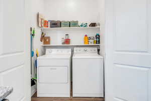 Clothes washing area with washer and clothes dryer, wood finished floors, and laundry area