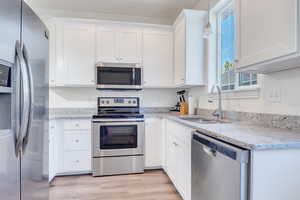 Kitchen featuring light wood-style flooring, white cabinetry, appliances with stainless steel finishes, light stone counters, and a sink