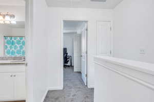 Hallway with light colored carpet, visible vents, attic access, a sink, and baseboards