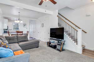 Living room with carpet floors, ceiling fan with notable chandelier, ornamental molding, and stairs
