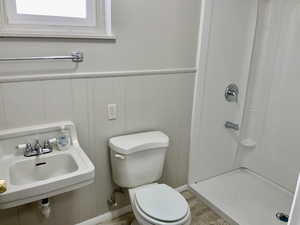Bathroom featuring a decorative wall, a sink, toilet, wood finished floors, and a stall shower