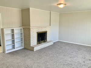 Unfurnished living room with wood walls, carpet flooring, and a brick fireplace