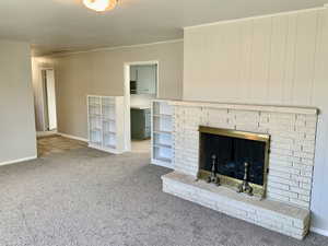 Unfurnished living room featuring crown molding, baseboards, carpet, and a brick fireplace