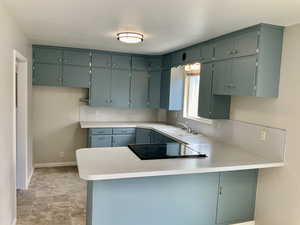Kitchen featuring light countertops, a peninsula, black electric stovetop, and a sink