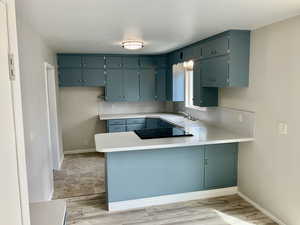 Kitchen featuring baseboards, a peninsula, light countertops, black electric cooktop, and a sink