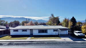 Ranch-style house featuring a mountain view, an attached garage, driveway, and a front lawn