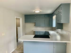 Kitchen with a peninsula, light countertops, a sink, baseboards, and black electric cooktop