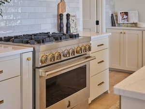 Room details with white cabinetry, high end range, and light stone counters