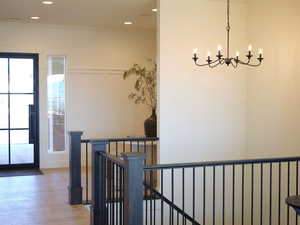Hall featuring light wood-style flooring, an upstairs landing, a chandelier, and a healthy amount of sunlight
