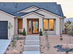 Exterior entry at dusk featuring an attached garage, concrete driveway, and stucco siding