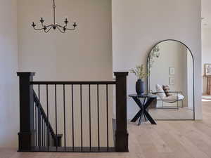 Corridor with arched walkways, a notable chandelier, an upstairs landing, and light wood-style floors