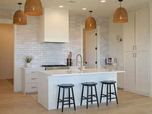 Kitchen featuring tasteful backsplash, light countertops, wall chimney exhaust hood, light wood finished floors, and a sink