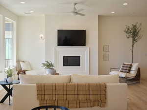 Living room featuring light wood finished floors, ceiling fan, a glass covered fireplace, and recessed lighting