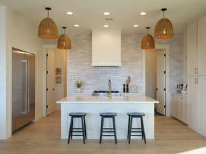 Kitchen featuring wall chimney range hood, a breakfast bar area, light countertops, and backsplash