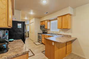 Kitchen with stainless steel appliances, a peninsula, a sink, visible vents, and light wood-style floors