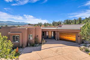 Pueblo-style house featuring a mountain view, a garage, a tile roof, stucco siding, and driveway