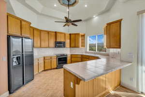 Kitchen with ceiling fan, a peninsula, appliances with stainless steel finishes, a high ceiling, and backsplash