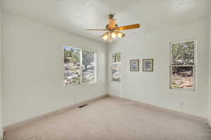 Carpeted empty room with visible vents, ceiling fan, and baseboards