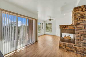 Unfurnished living room featuring baseboards, a fireplace, visible vents, ceiling fan, and wood finished floors