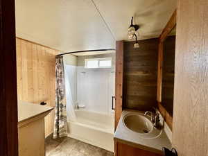 Bathroom featuring shower / tub combo, a textured ceiling, wood walls, and vanity
