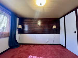 Carpeted spare room featuring wood walls and baseboards