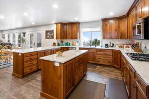 Kitchen featuring dark wood-style flooring, a peninsula, stainless steel appliances, and brown cabinetry