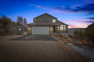 View of front of house with driveway, a standing seam roof, brick siding, a storage unit, and an attached garage