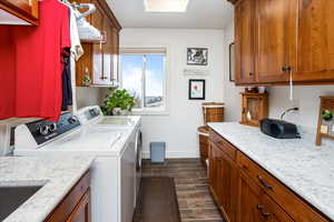 Laundry room with wood tiled floor, washer and clothes dryer, cabinet space, and baseboards