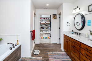 Full bathroom with vanity, wood finish floors, baseboards, visible vents, and a bath